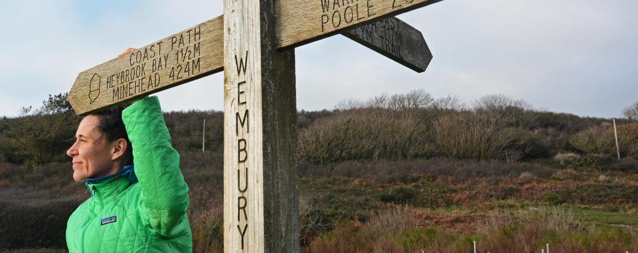 Emma Hazeldine beside a South West Coast Path signpost at Wembury, Devon